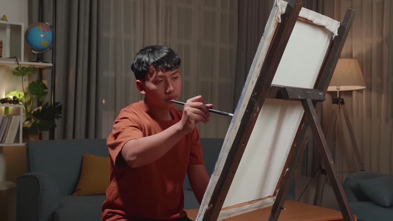 Asian Artist Boy Holding Paintbrush Mixed Colour And Painting On The Canvas
