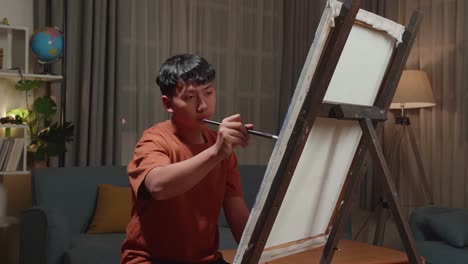 Asian Artist Boy Holding Paintbrush Mixed Colour And Painting On The Canvas