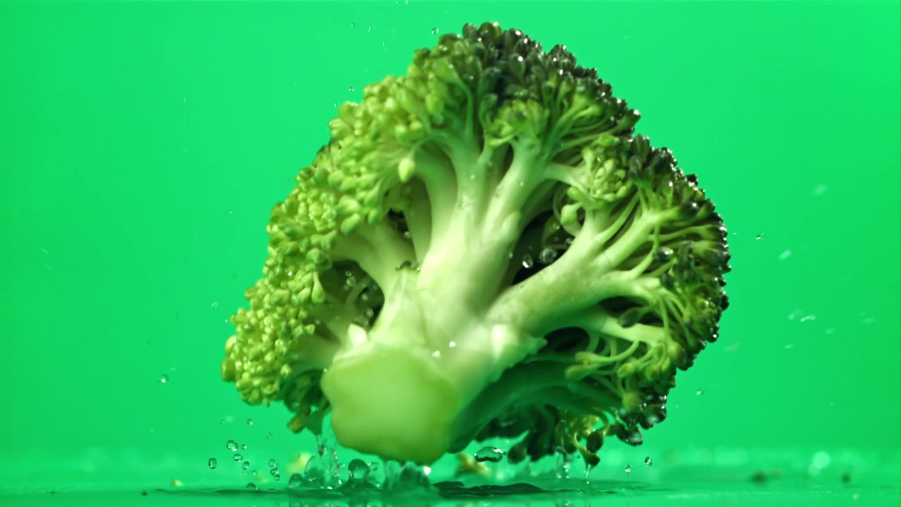 Broccoli freschi che cadono e schizzano acqua su schermo verde al rallentatore