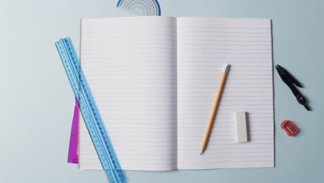 overhead view of open notebook with school stationery on blue background, in slow motion