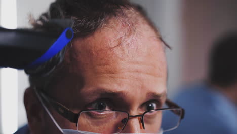 concentrated-man-in-glasses-cuts-hair-on-head-with-trimmer