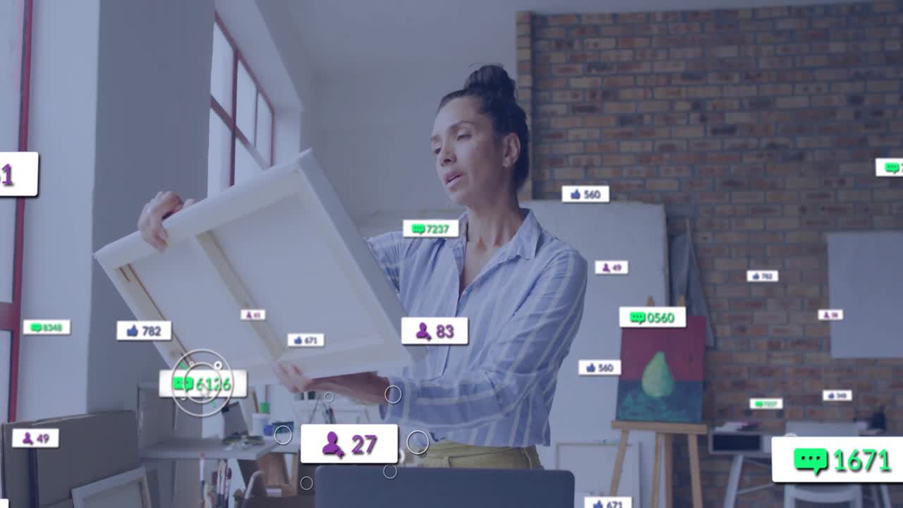 Mature artist lifting canvas toward window while monitoring social media viewer counts and likes