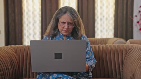mujer india de edad que tiene dolor en el ojo después de trabajar en la computadora portátil