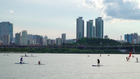 locals and tourists paddle boarding on han river with asem tower at background in seoul, south korea