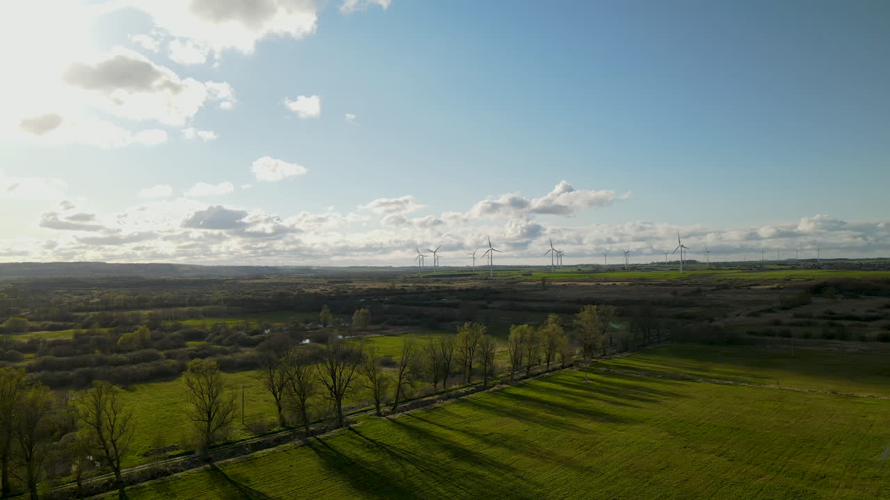 공중 드론은 봄에 푸른 들판과 나무 줄 위로 날아가고, 퍽에 있는 풍차 농장 공장, 맑고 흐린 날 폴란드