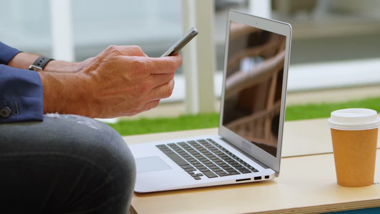 uomo d'affari che usa un telefono cellulare mentre lavora su un laptop 4k