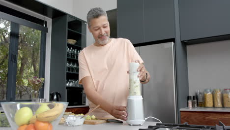 hombre bi-racial feliz mezclando batido saludable en la cocina, espacio de copia, cámara lenta