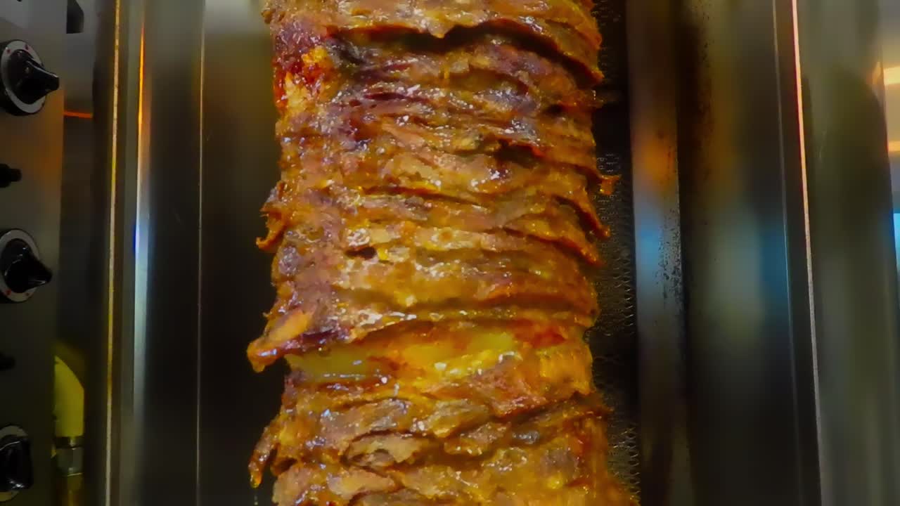 bucle continuo 2 de 5 primer plano de bistecs apilados cortados en rodajas finas sobre una barbacoa vertical marinada y los jugos fluyendo hacia abajo con la carne de res shawarma de estilo árabe en un asador de acero inoxidable cocinando lentamente