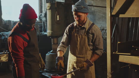 blacksmith explaining how to shape red-hot iron to colleague in workshop