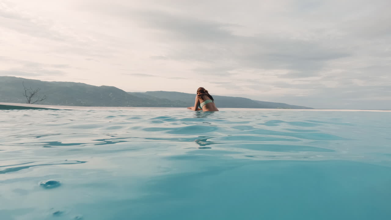 Junge Frau genießt herrliche Aussicht aus einem riesigen Infinity-Pool.
