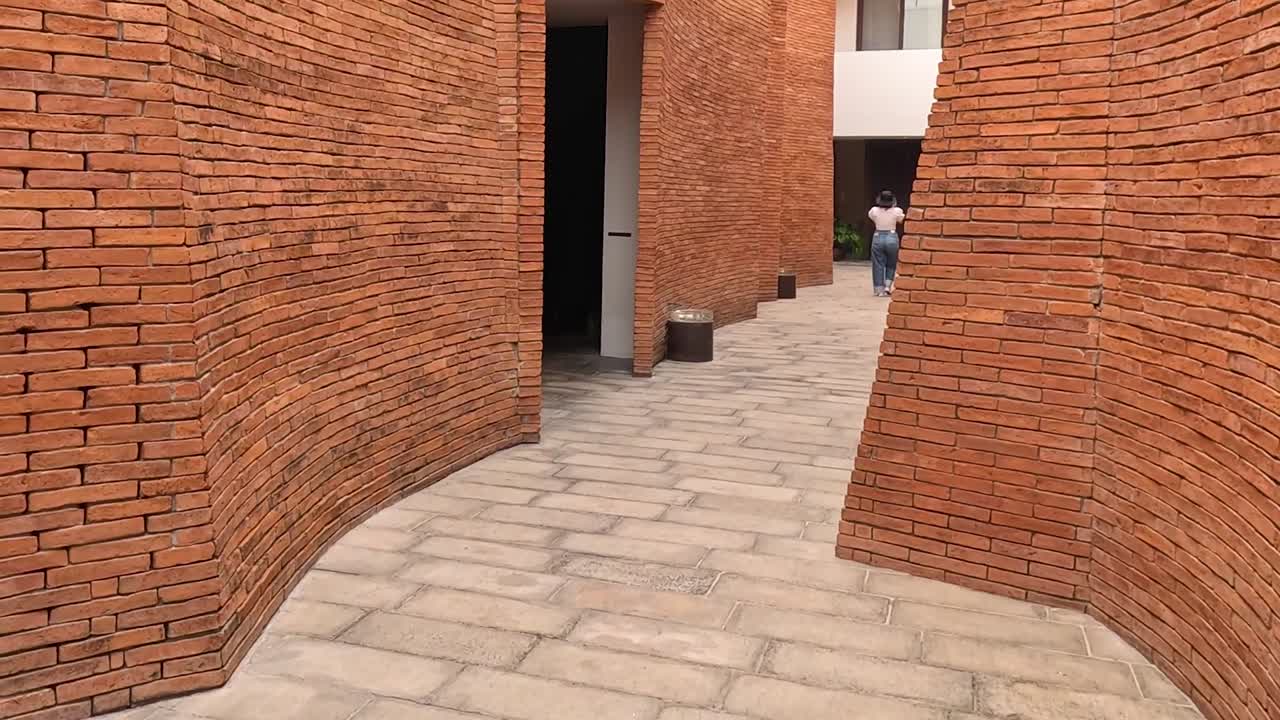 Explore the intricate curves of red brick walls and paved pathways in an urban architectural space.