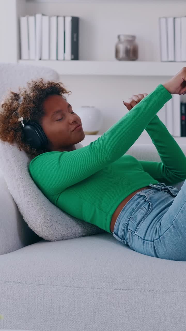 Young woman with headphones relaxing on a sofa scrolling a smartphone at home