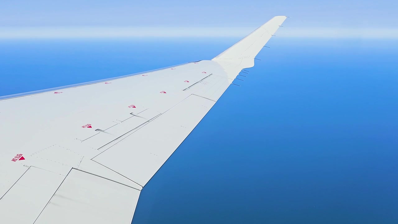 飛行機の窓からの視点。青い海と空の上を飛ぶ白い航空機の翼、水平線の上をゆく高高度飛行。旅行、休暇、航空、交通、空撮の背景映像。