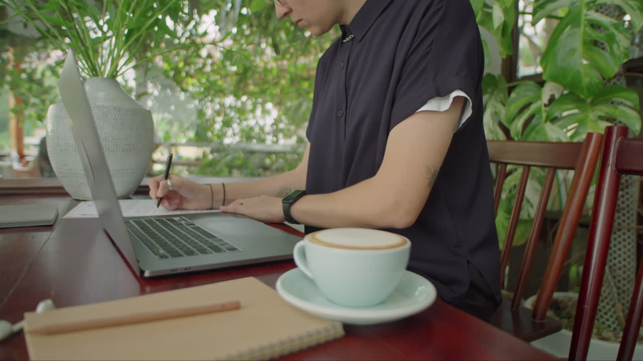 Woman Working on Laptop and Making Notes in Outdoor Cafe