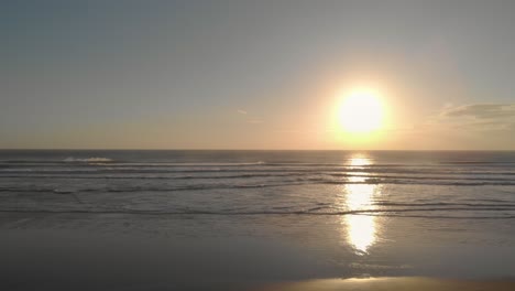 flying low and slowly from a soft sandy beach towards a wild ocean at sunset