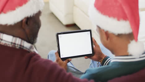 happy african american father and adult son in christmas hats using tablet, copy space, slow motion
