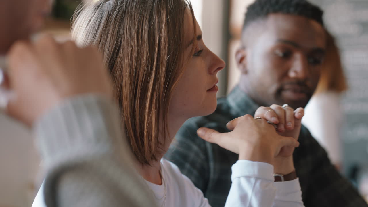젊은 백인 여성이 웃는 얼굴을 짓고 어리석은 표정을 짓고 카페에서 친구들과 어울려 재미를 즐기고 있습니다.