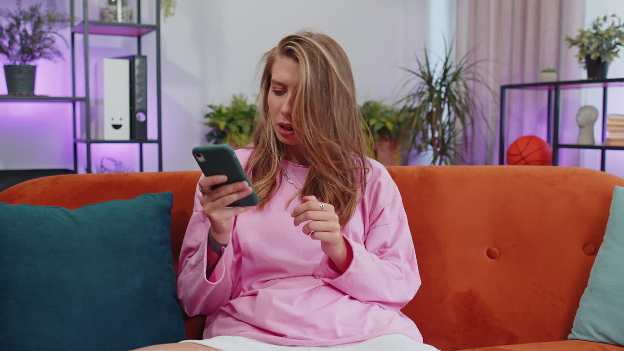 소파에 앉아있는 젊은 여성의 초상화, 스마트폰을 사용하여 소셜 미디어 응용 프로그램에서 메시지를 공유합니다.