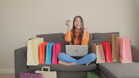 beautiful asian woman celebrating in front of laptop on couch