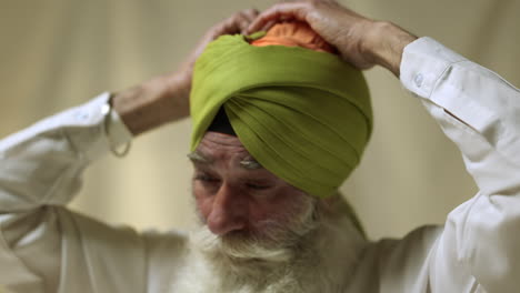 Primer-Plano-De-Estudio-De-Un-Hombre-Sikh-Mayor-Con-Barba-Atando-Tela-Para-Un-Turbante-Contra-Un-Fondo-Liso,-Filmado-En-Tiempo-Real-1