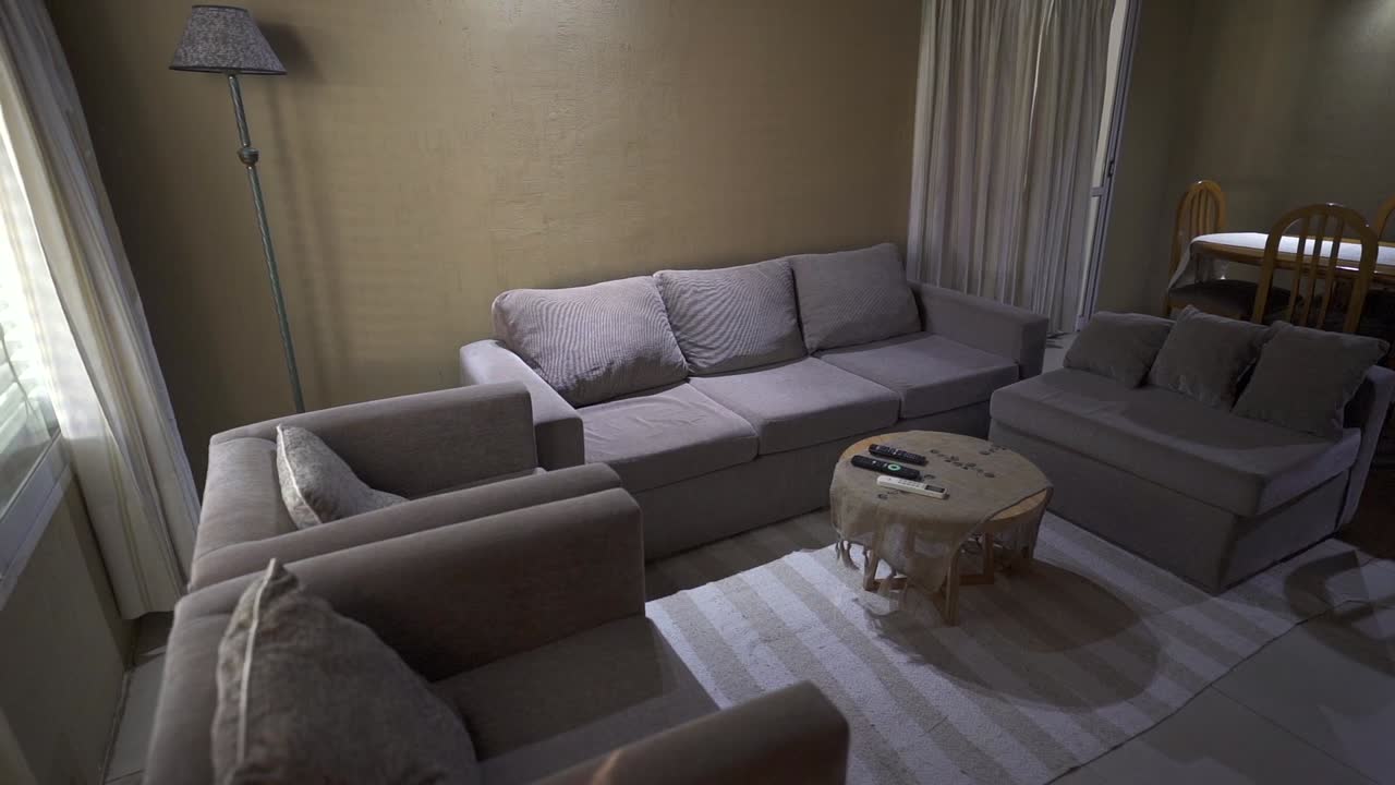 Alternate panning view of cozy wooden house living and dining room, with couch and surroundings in grey and brown tones. Shot on 4K.