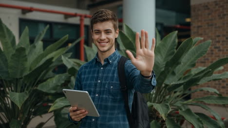 young man waving and smiling with a tablet