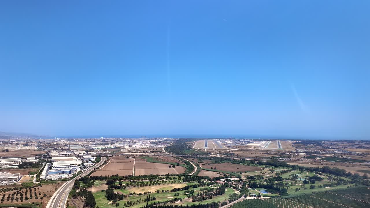 Aerial cockpit view from inside a jet cockpit approaching to Málaga airport, the coastline fading into blue, and two parallel runways stretching toward the horizon. Bright and sunny summer day