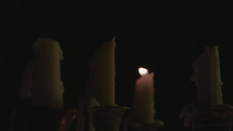 A-close-up-of-a-group-of-melted-white-candles-on-a-candelabra-and-all-of-them-but-one-get-blown-out-by-the-wind