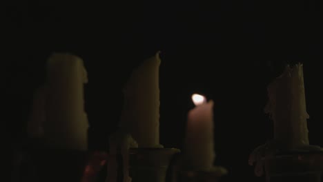un primer plano de un grupo de velas blancas derretidas en un candelabro y todas menos una son apagadas por el viento