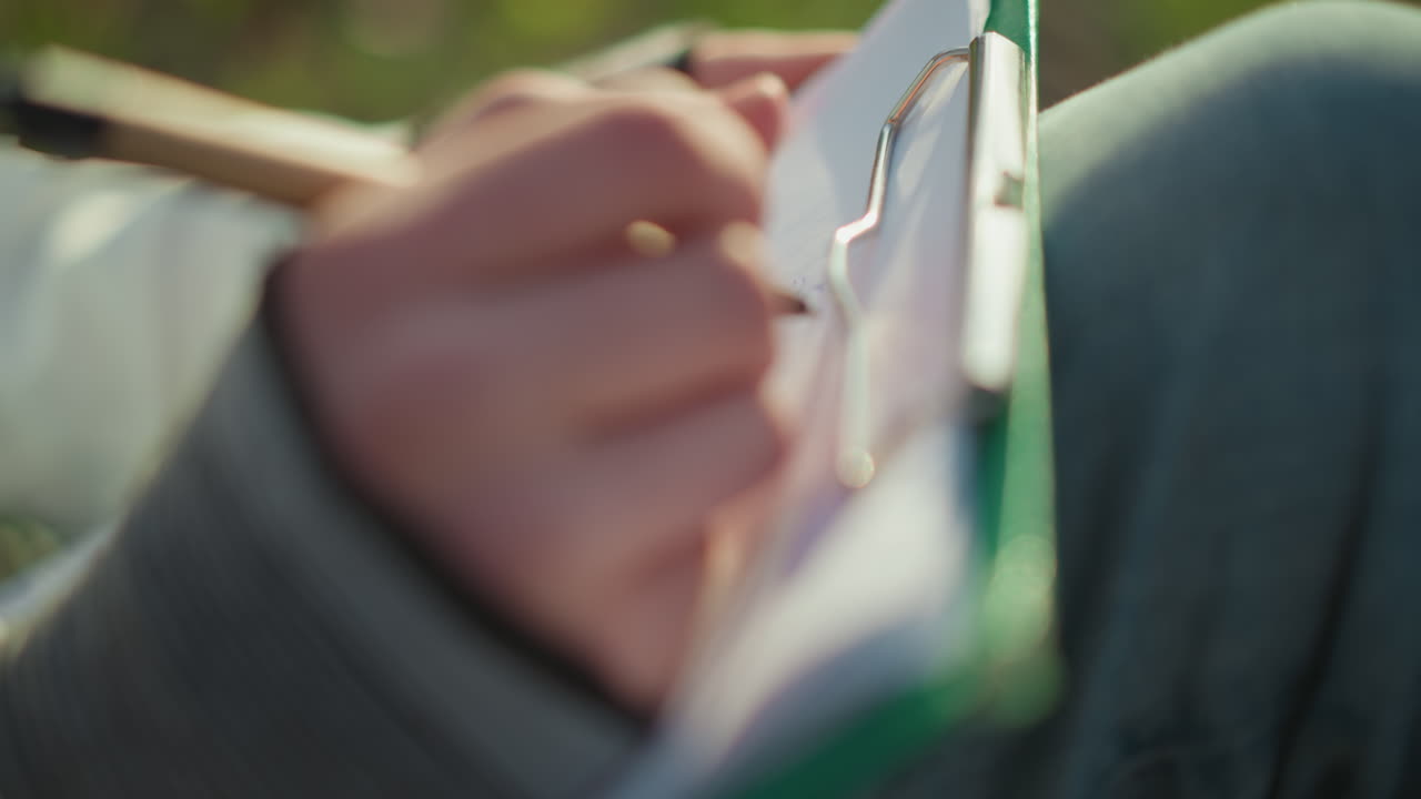 펜을 빠르게 움직여 그림을 그리는 십 대 소녀, 햇빛 아래 야외에서 예술 작품을 만드는 청소년의 클로즈업 뷰, 햇빛이 비치는 공원 환경에서 스케치하며 강렬하게 집중하는 젊은이