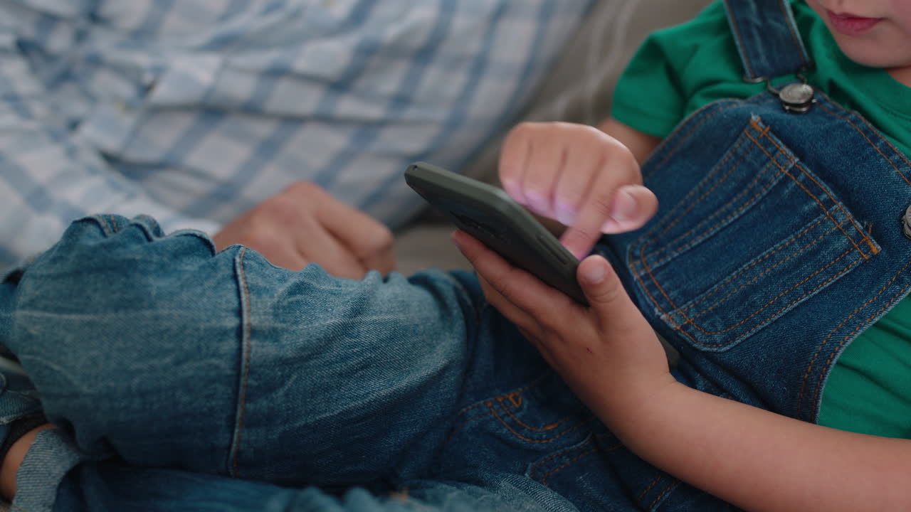 happy grandfather showing little boy how to use smartphone teaching curious grandson modern technology intelligent child learning mobile phone sitting with grandpa on sofa