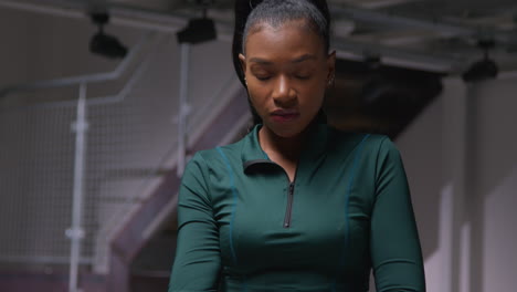 portrait of determined female athlete wearing tracksuit training in gym stretching and warming up preparing for sports event