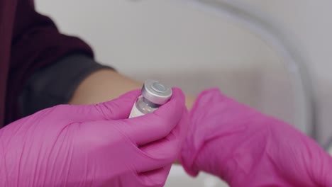 manos del médico o de la enfermera con guantes de látex vistos abriendo un vial o ampolla para el tratamiento con botox - cámara lenta aislada