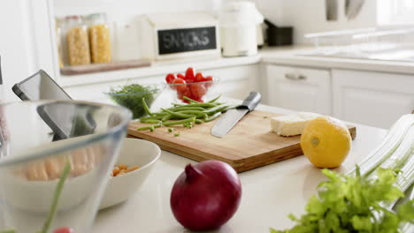 knife, cutting board, vegetables and tablet on counter in sunny kitchen, slow motion