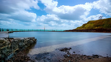 Tiro-De-Hiperlapso-De-Nubes-Voladoras-Sobre-La-Piscina-De-La-Playa-En-Guernsey-Con-Vista-Al-Mar-En-Segundo-Plano