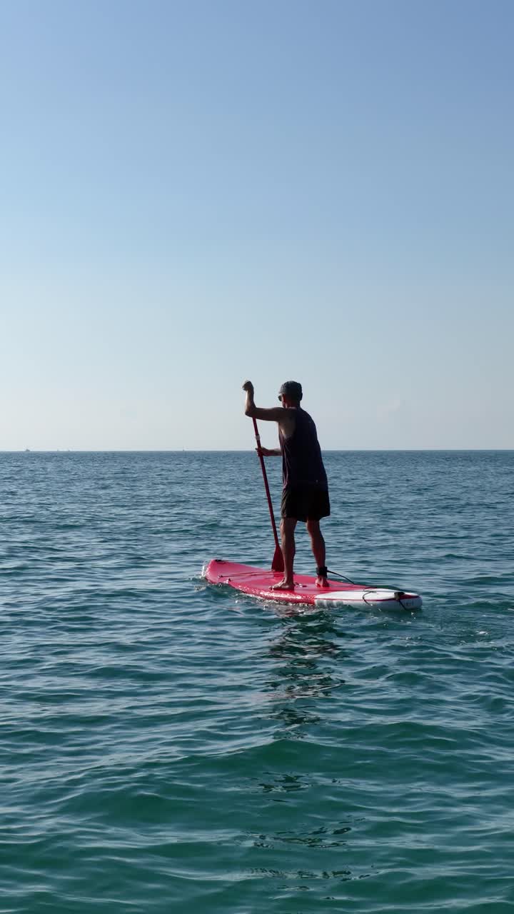 Sportsman paddling on sup board in calm sea. Vertical