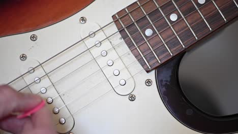 4k video of a close-up of a man's hand plucking the strings of an electric guitar with a pink plectrum