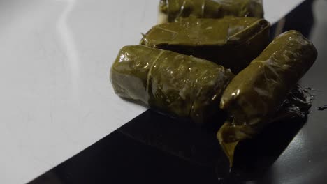 dolmades envueltas en hojas de uva que gotean con aceite de oliva, colocadas en una bandeja