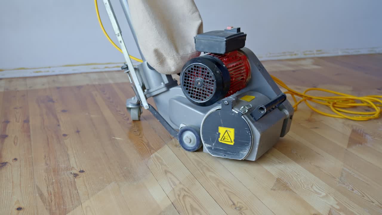 Floor sanding machine stands on sanded surface showing before and after floor refinishing