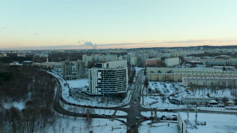 La-Tarde-Desciende-Sobre-Un-Barrio-Urbano-Cubierto-De-Nieve-Con-Un-Edificio-Moderno-Prominente-Y-Una-Carretera-Curva-Que-Atraviesa-La-Zona-Residencial.