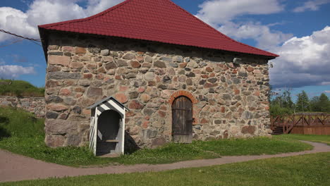 an outside view of a hall of an old fortress made of stones with a small gate, red tiles top, russia