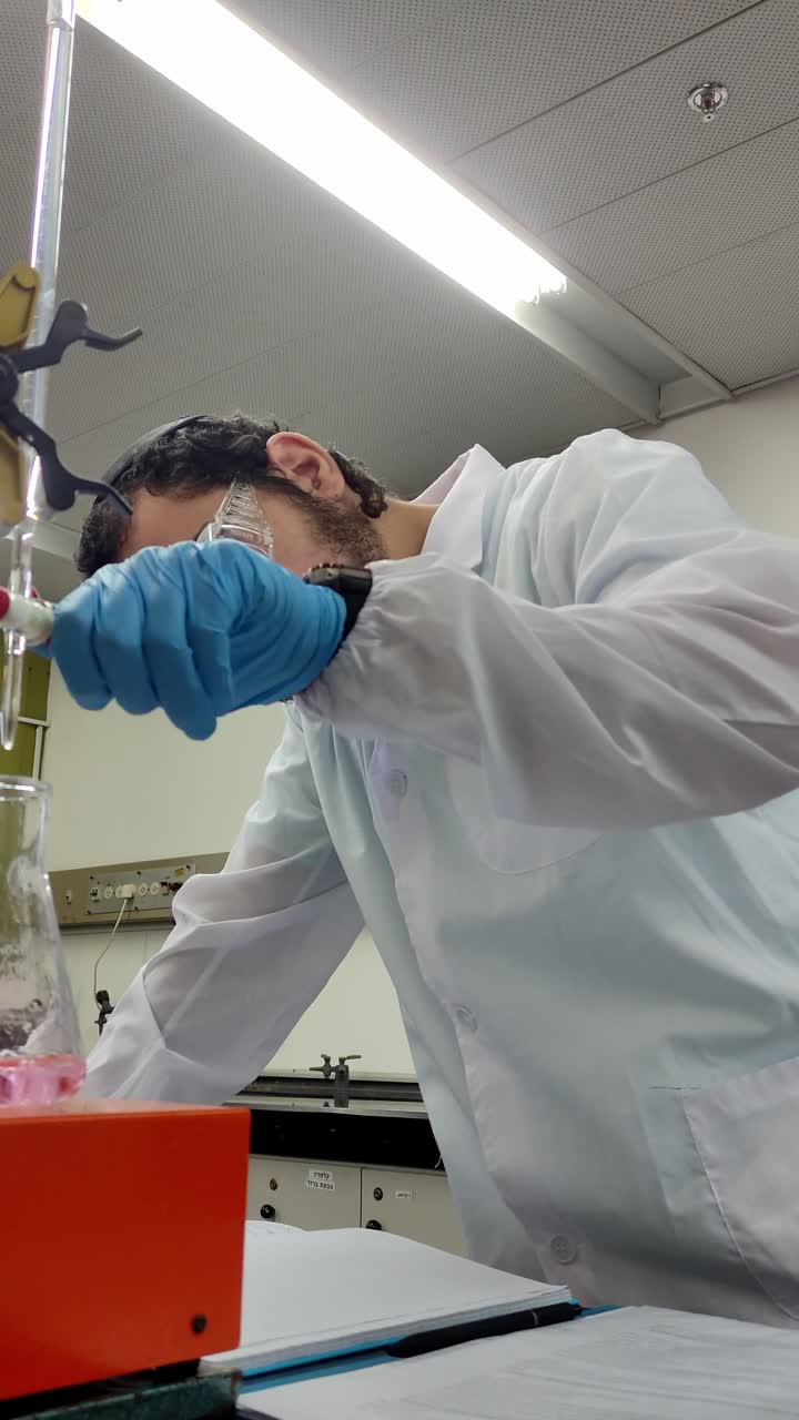 A man in a lab coat is wearing gloves and looking at a beaker