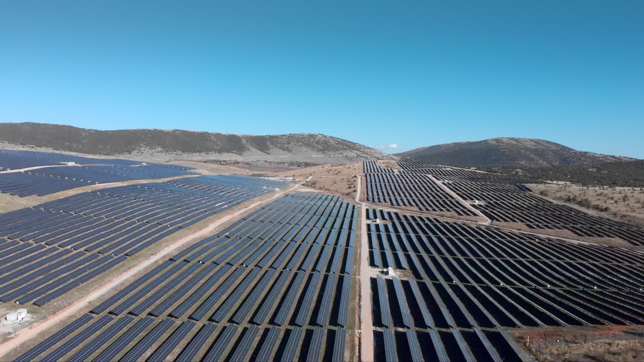 Drone over en kæmpe fotovoltaisk solcellepark med rækker af paneler på bakker, panorerer ned