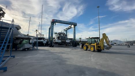turkey,marmaris, marina, a big crane is parking a huge motor yacht very slowly at a marina's parking on land, a yellow caterpillar is waiting for the process to be completed.a regular day at a marina