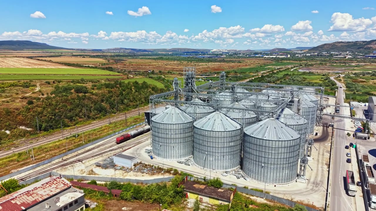 Large storage silos and rail tracks in an agricultural area under a blue sky with clouds during daylight