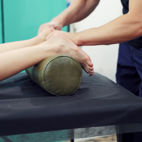 woman's legs lying on a roller on the black table and massagist doing massage on barefoot outside. male masseur is doing acupressure to a female's feet in the open air.