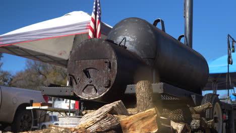 Low-Angle-of-an-off-set-BBQ-Smoker-with-a-pile-of-oak-logs-in-front