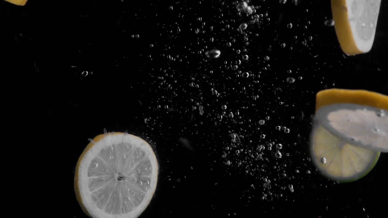 Lemon and Lime Slices Falling into Water Super Slowmotion, Black Background, lots of Air Bubbles, 4k240fps