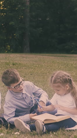 classmates sit on school yard grass lawn read books discuss home assignment and eat sandwich close view slow motion