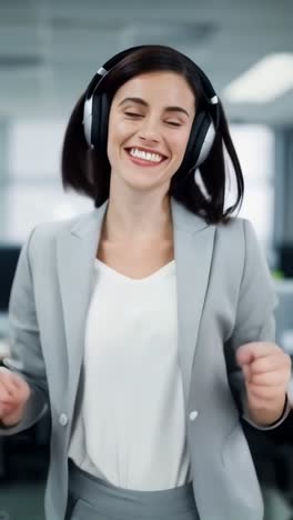 a happy young businesswoman wearing headphones and gray suit, joyfully dancing in an office.